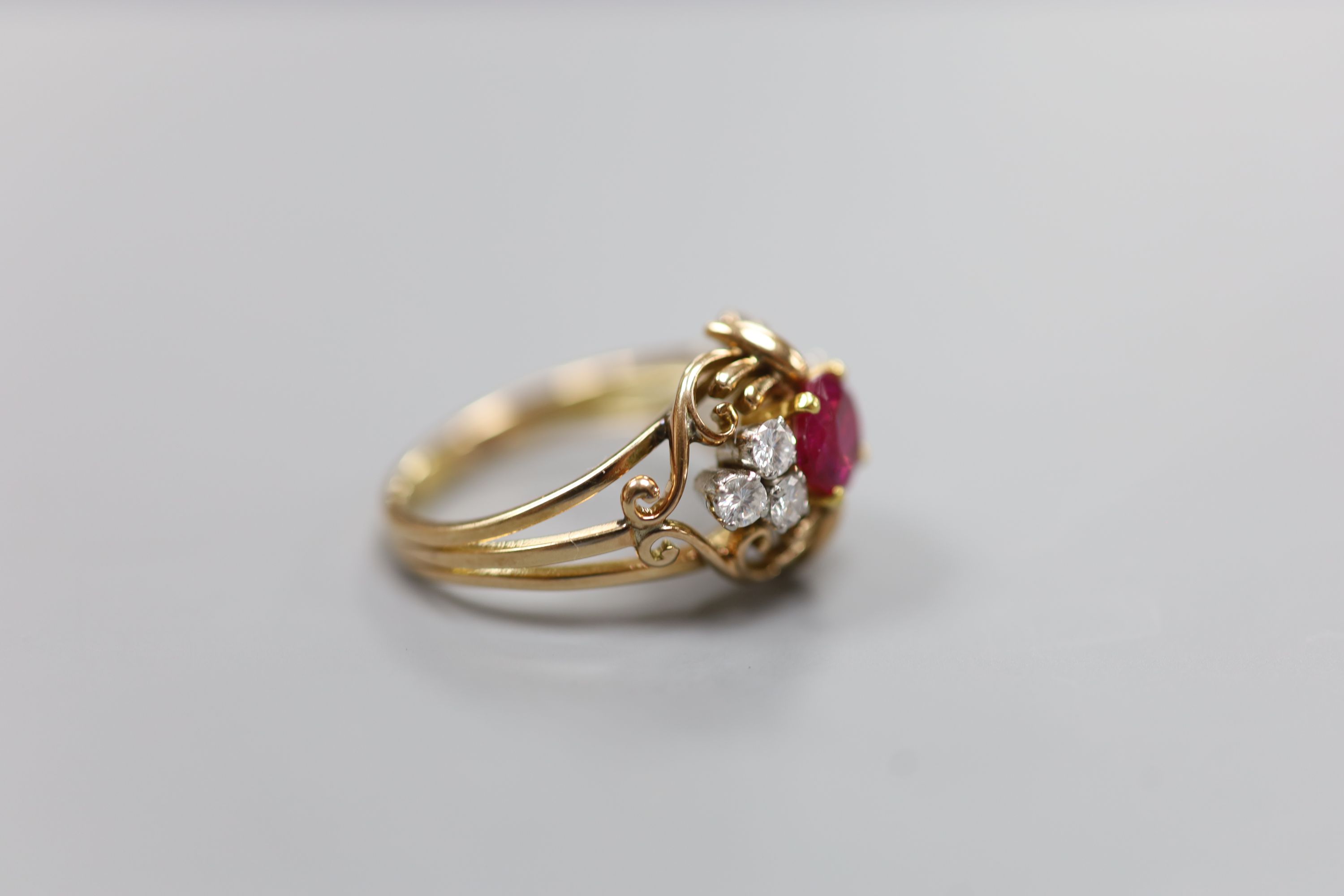 A stylish yellow metal, ruby and diamond set cluster ring, with single round cut ruby(crack), flanked by six round cut diamonds, in an openwork scroll setting, size Q/R, gross weight 7.5 grams, in a Cartier box.